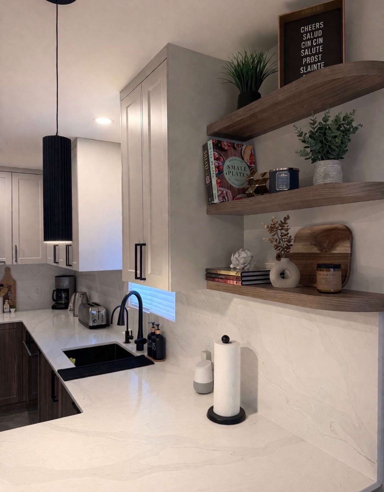 Détail des tablettes flottantes en noyer arrondi au-dessus du plan de travail, avec plantes, livres et bougies.