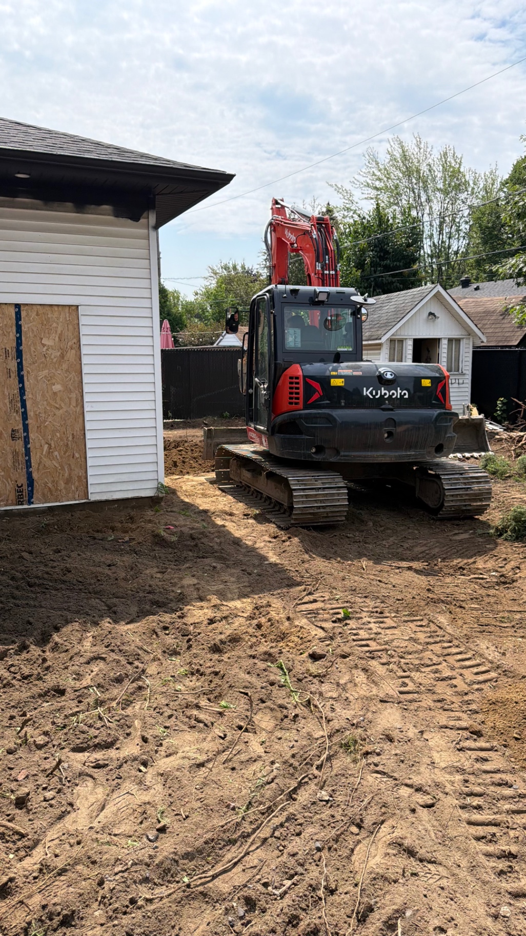 Excavatrice Kubota positionnée entre les bâtiments existants, terrain nivelé pour recevoir la nouvelle fondation.