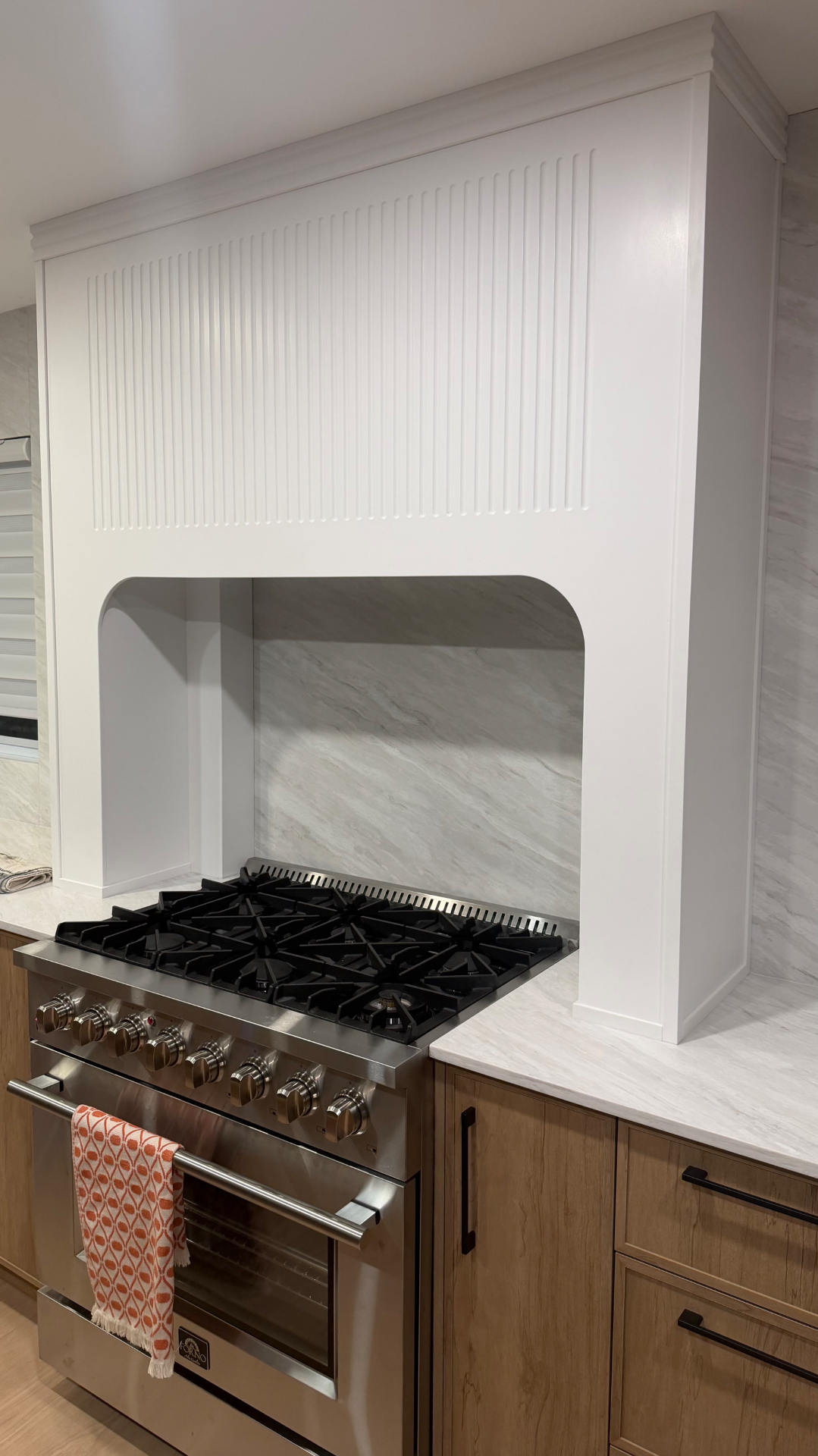 Détail de la hotte cannelée blanche pleine hauteur au-dessus de la cuisinière professionnelle, dosseret en marbre veiné.