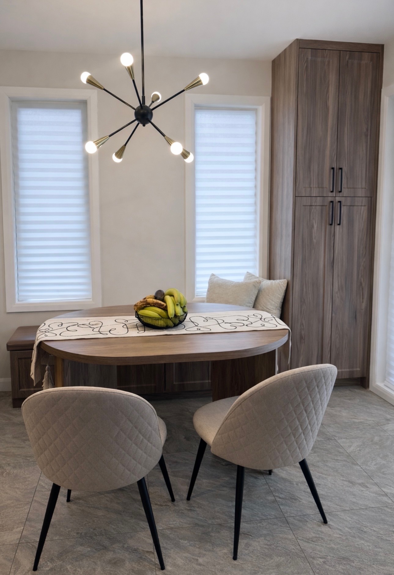 Coin repas avec banquette sur mesure, chaises capitonnées, lustre sputnik laiton et noir, colonne de rangement en noyer.
