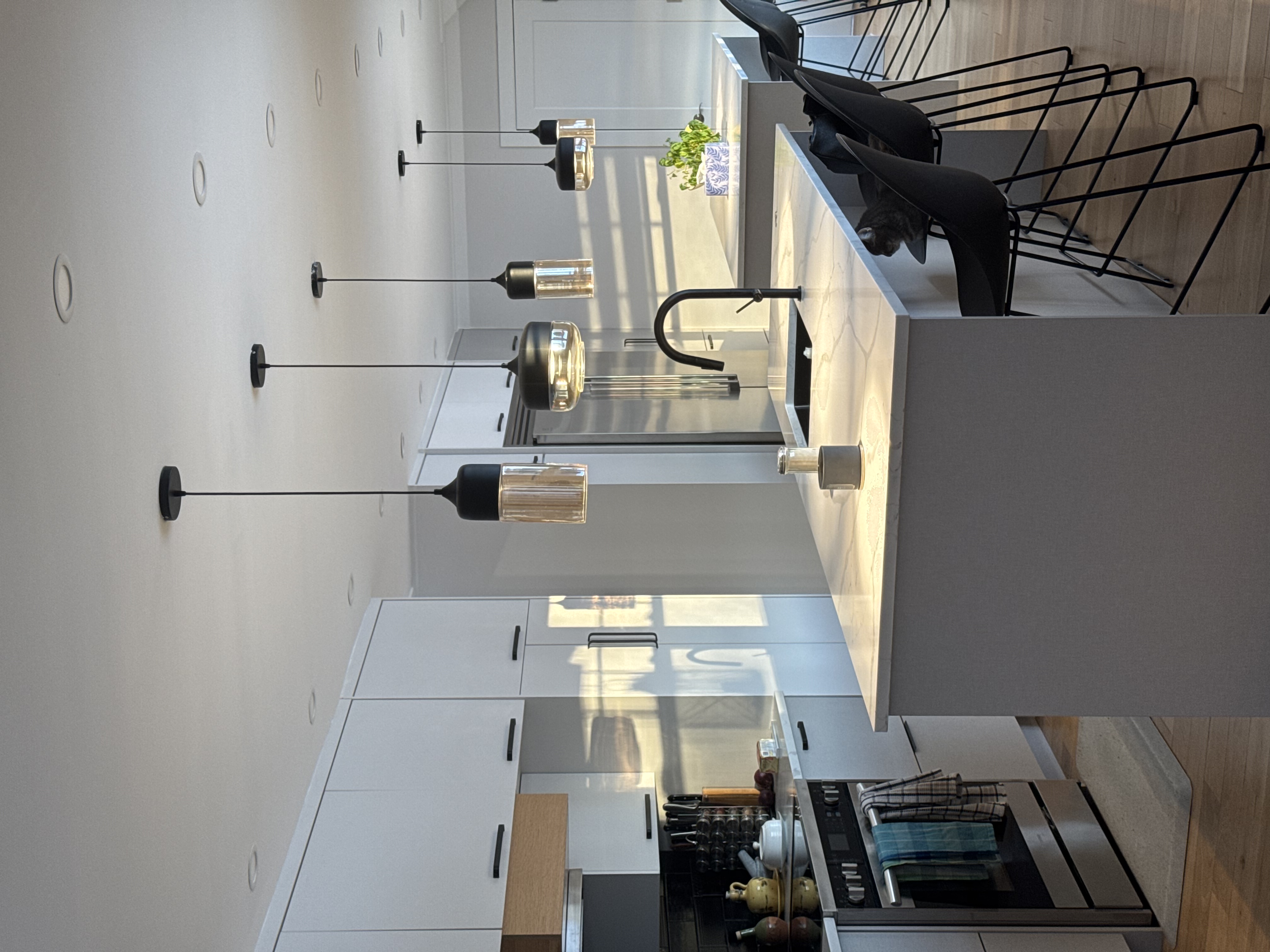 Coin cuisson de la cuisine secondaire, agrandissement Belmont — comptoirs blancs et suspensions noires.