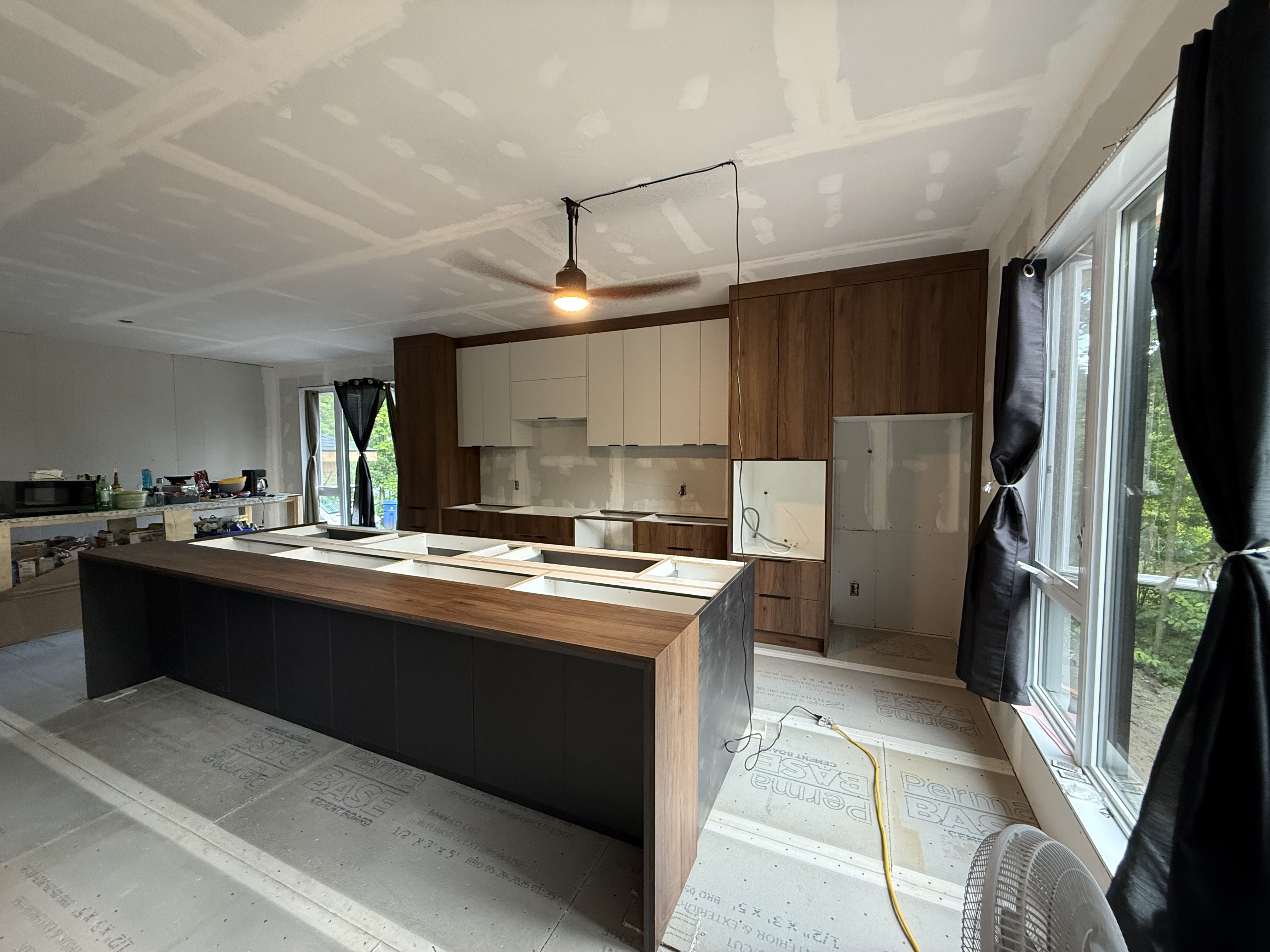Cuisine en chantier à Lachute — armoires en placage de noyer et caissons cashmere gold, grand îlot central avec comptoir en noyer, plafonds de 9 pieds.