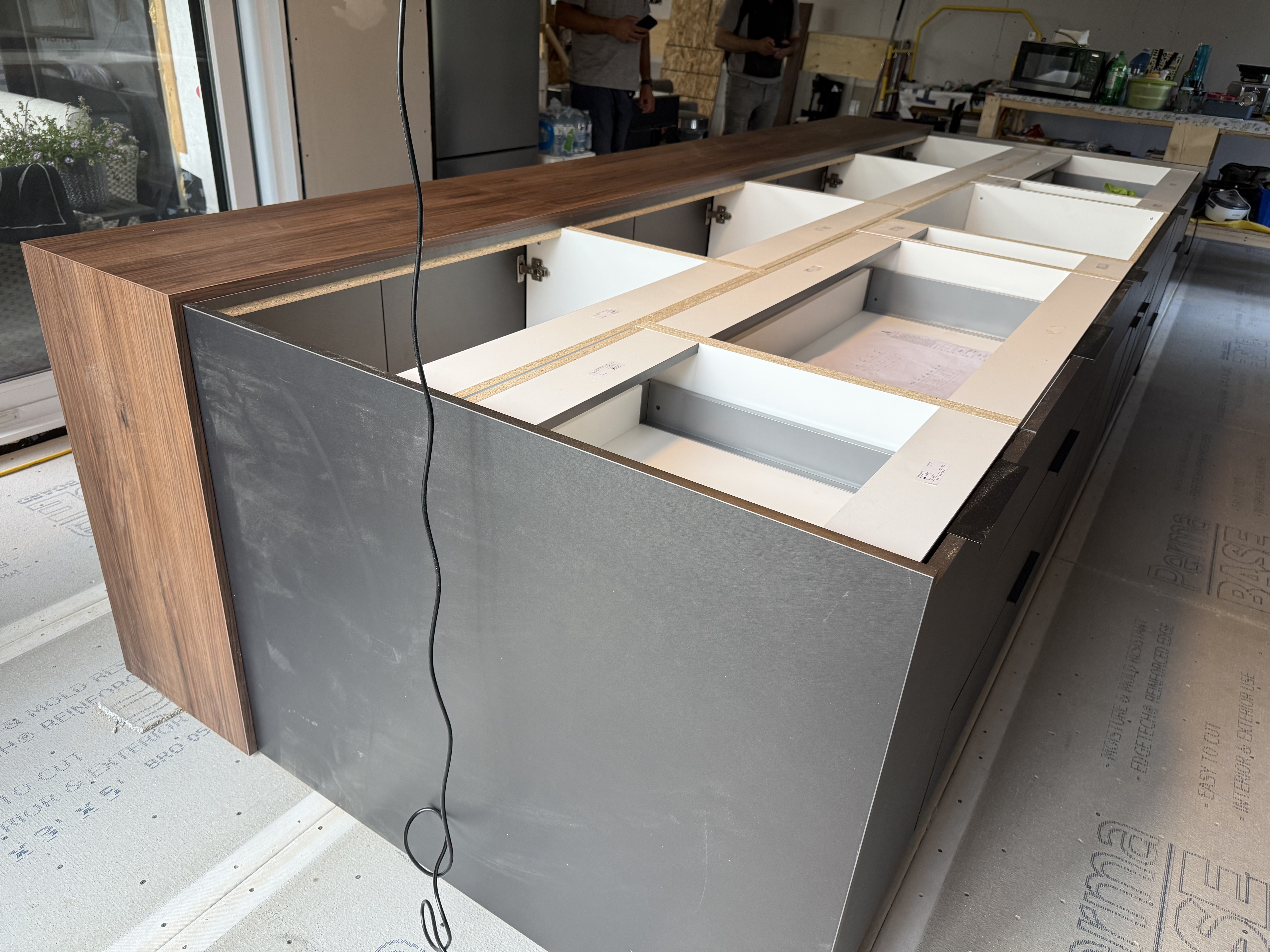 Détail de l'îlot en cours d'assemblage — comptoir en noyer à effet cascade et caissons gris anthracite.