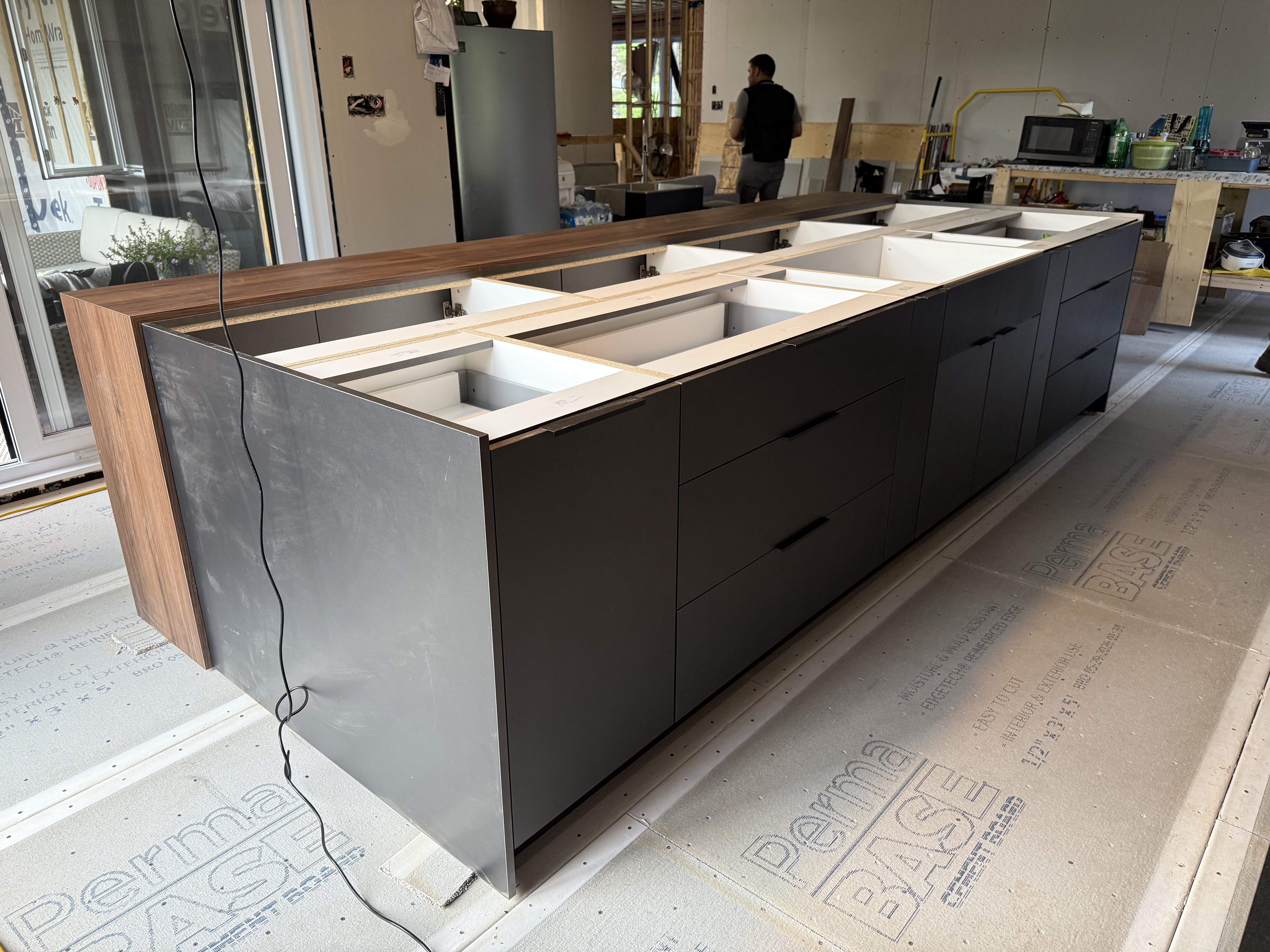 Longue vue de l'îlot en chantier avec tiroirs gris anthracite et comptoir en noyer.