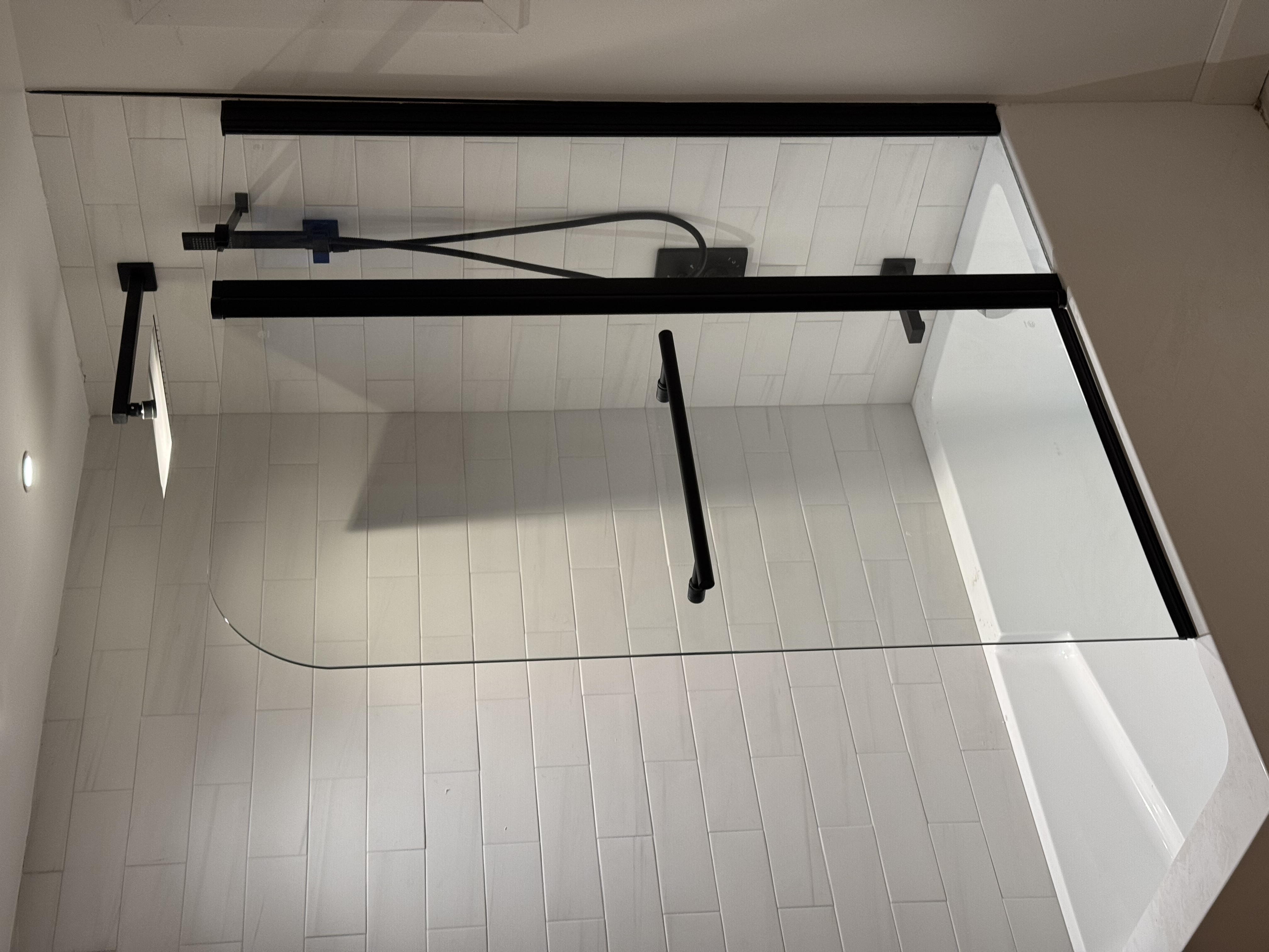 Douche en verre sur mesure à Laval, paroi courbe, quincaillerie noir mat et robinetterie Evos Boutiques, céramique blanche en format long.
