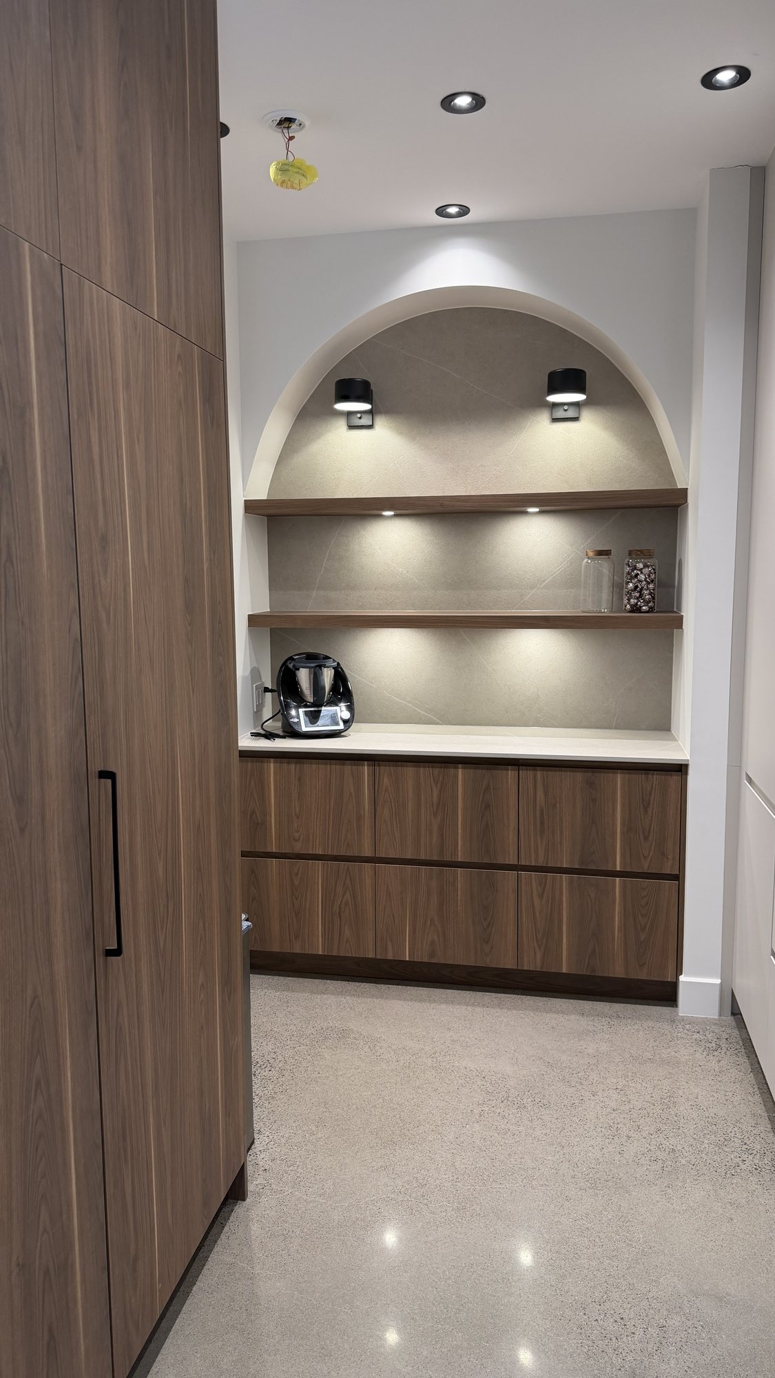 Pantry in the 30th Avenue Project — arched Dekton niche with recessed lighting under walnut-veneer shelves, AGT PET cabinet boxes.