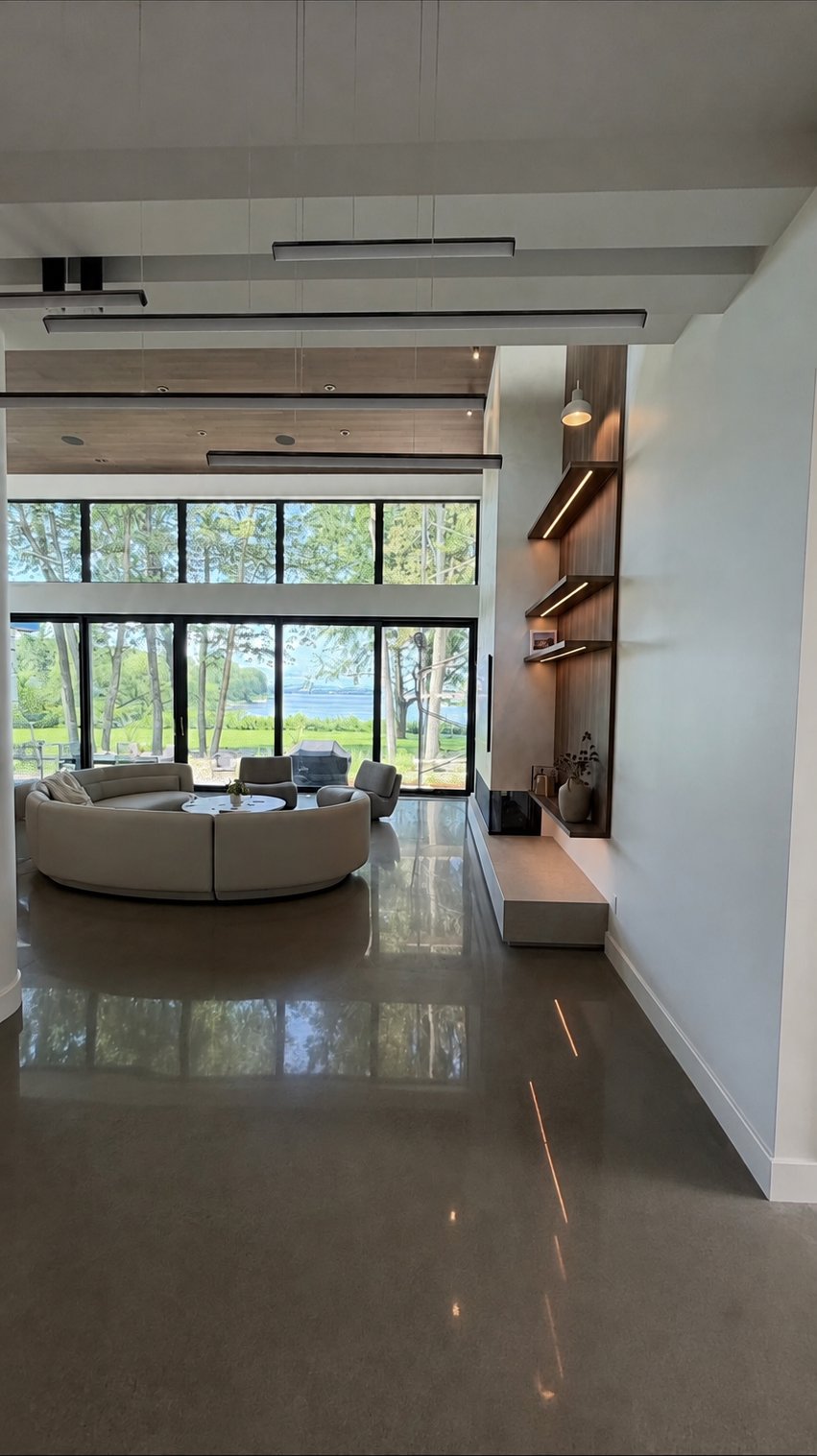 Great room in the 30th Avenue Project — walnut-veneer storage wall with lit shelving, open view over the grounds and trees.