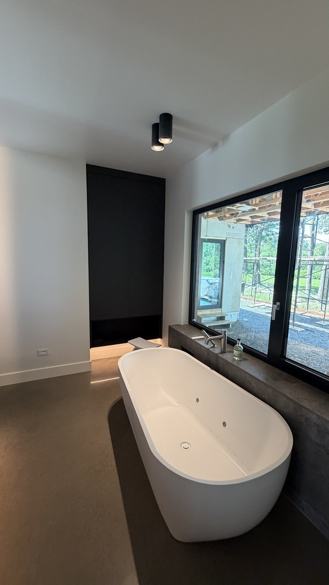 Primary suite bathroom, 30th Avenue Project — freestanding tub under a large window, matte-black storage column.
