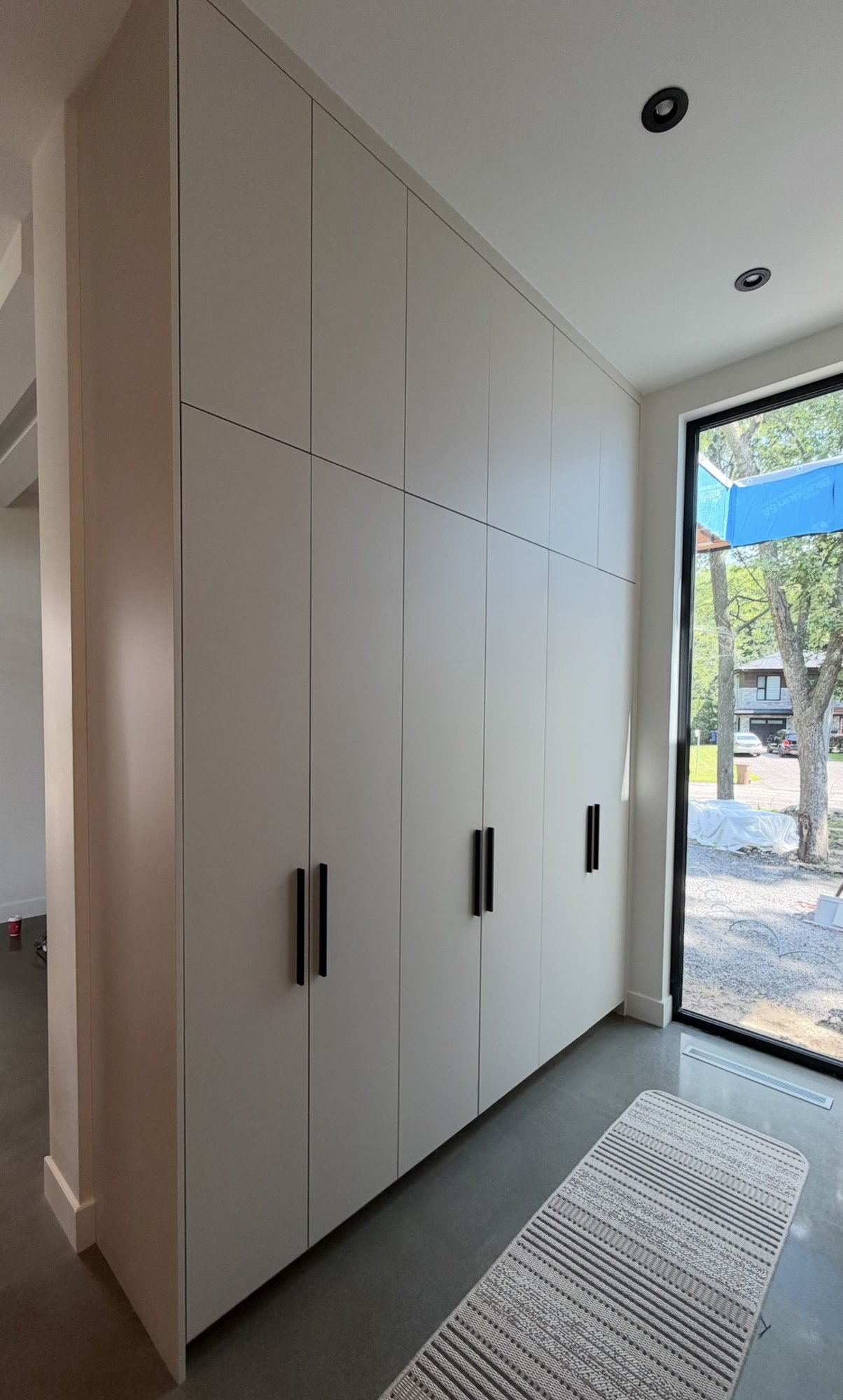Storage wall in the mudroom, 30th Avenue Project — white AGT PET columns with black handles, full-height glazed door behind.