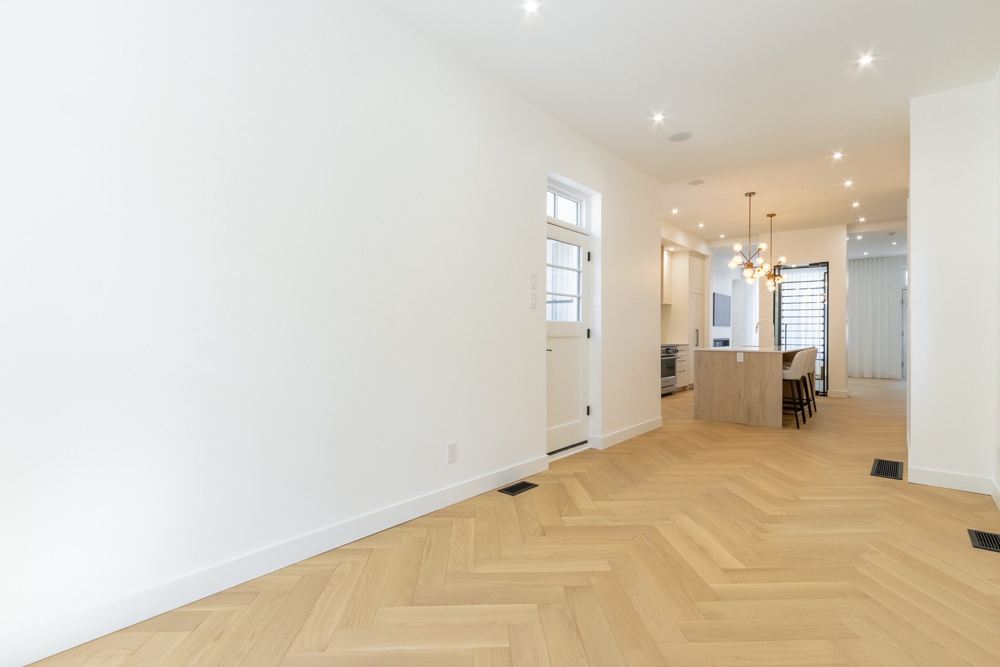 Herringbone oak hallway leading to the open kitchen, with the glazed wine cellar and brass chandelier visible beyond.