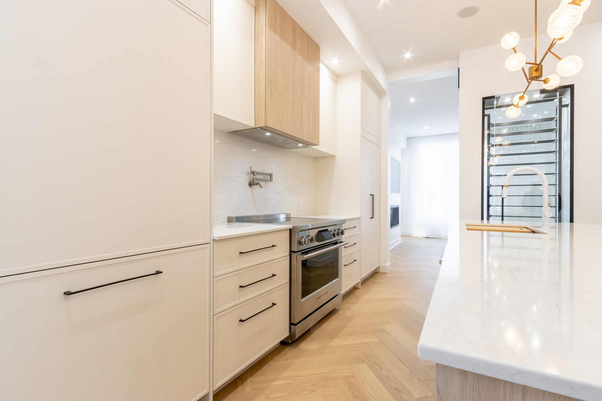 Range wall of the Westmount kitchen — veined-marble backsplash, oak-veneer hood, pro range and glazed wine cellar behind.