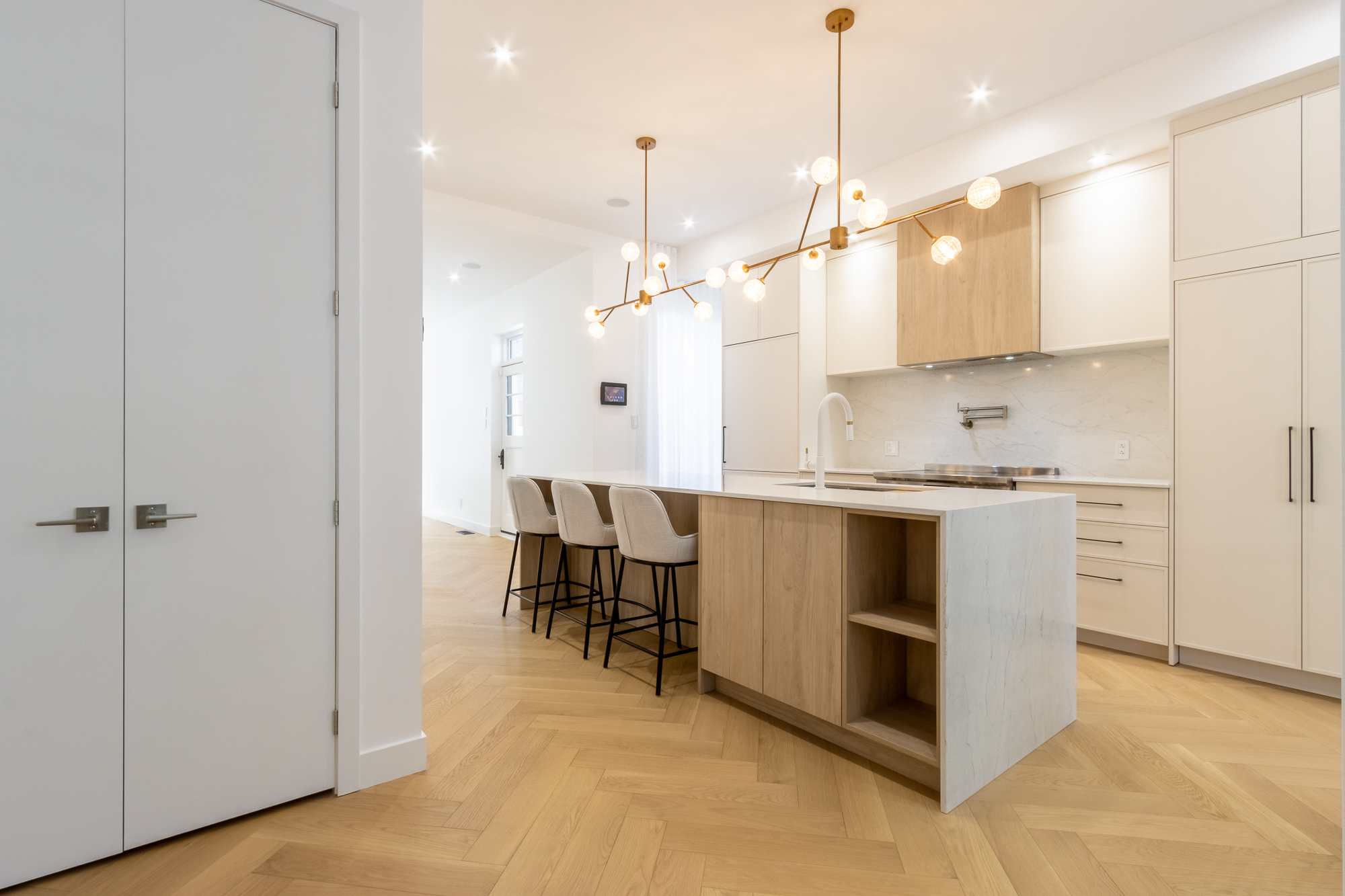 Waterfall quartz island with integrated open shelving and upholstered stools, Atelier Pelissier custom kitchen in Westmount.