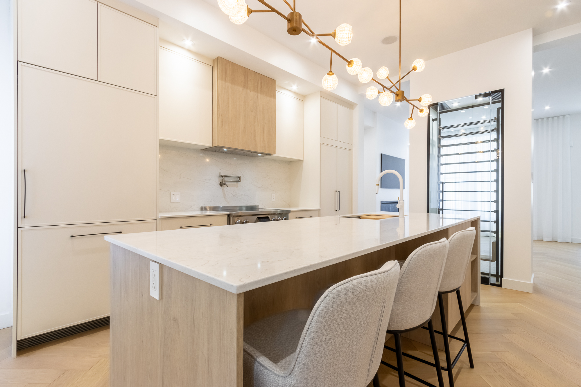 Wide view of the Atelier Pelissier custom kitchen in Westmount — off-white pantry columns, oak-veneer hood and quartz waterfall island.
