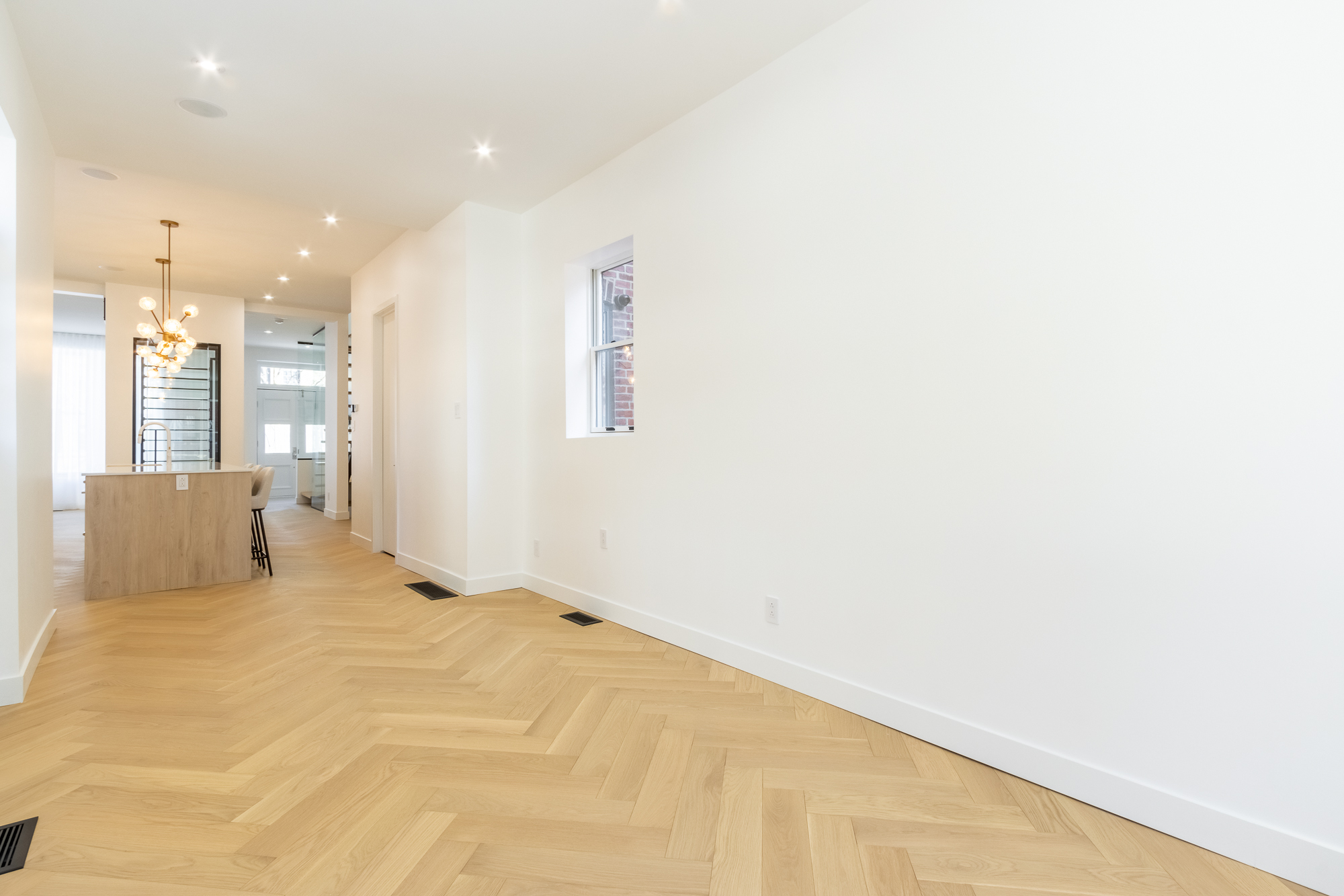 Entry of the Westmount home with a full-height glazed door, herringbone oak flooring and a view through to the kitchen.
