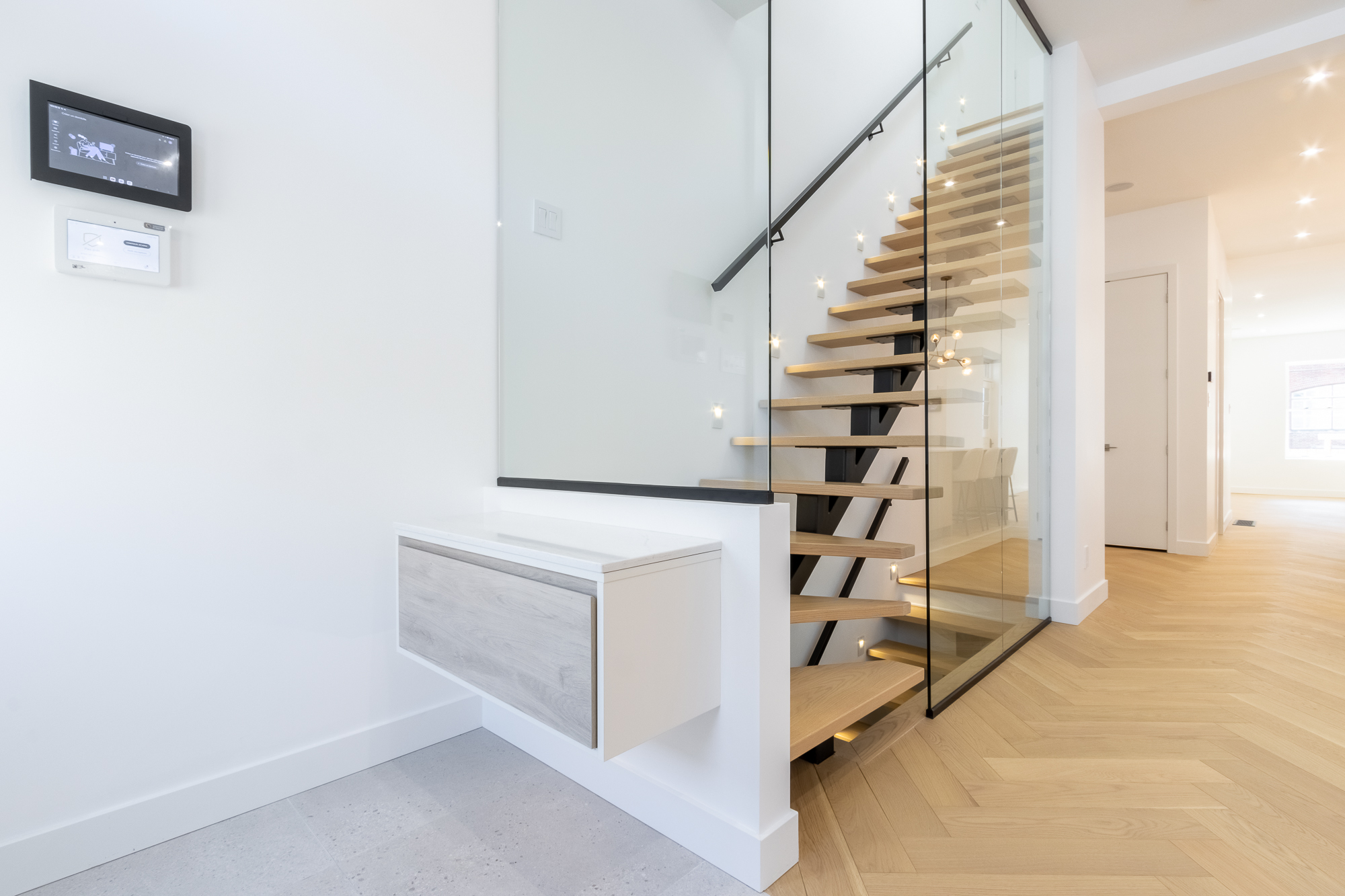 Floating oak-and-black-steel staircase behind a full-height glass wall, Westmount residence.