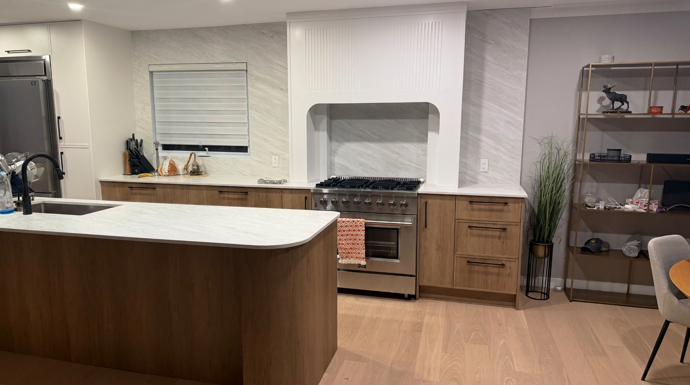 Vue élargie de la cuisine Belmont — îlot en chêne, comptoirs en marbre veiné, colonnes de rangement et étagère en laiton à droite.